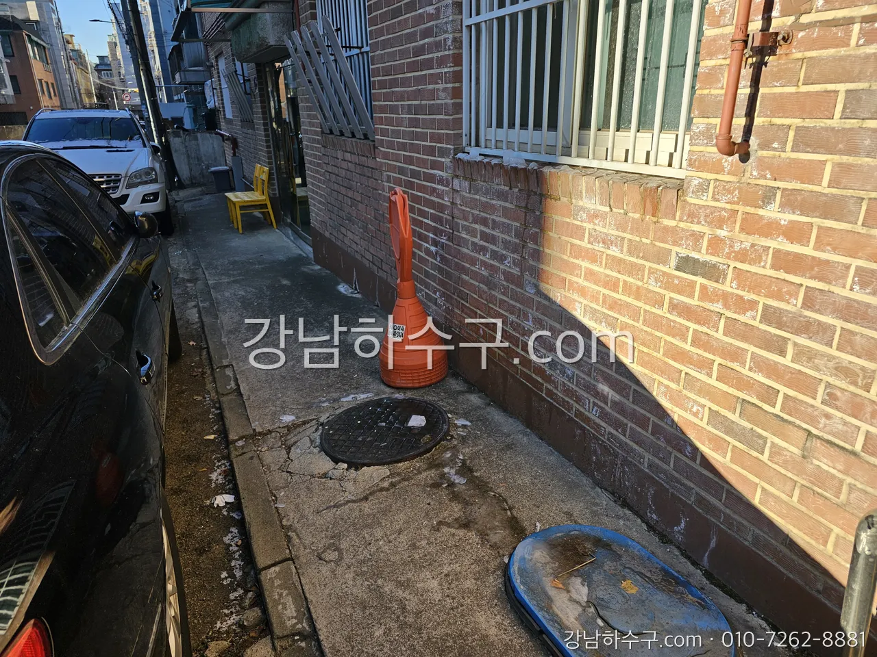 겨울 상가주택 옆 골목의 맨홀 뚜껑 — 얇은 뚜껑 아래 물이 얼면 집수정 펌프 플로트가 갇힙니다
